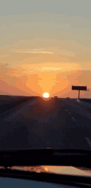 the sun is setting over the highway with a billboard in the background