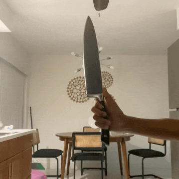 a person is holding a large knife in front of a dining room table