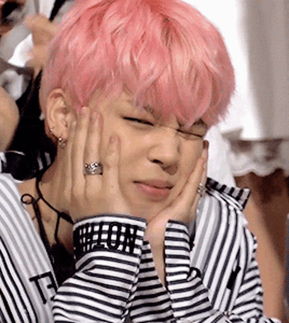 a man with pink hair is wearing a striped shirt and holding his face with his hands .