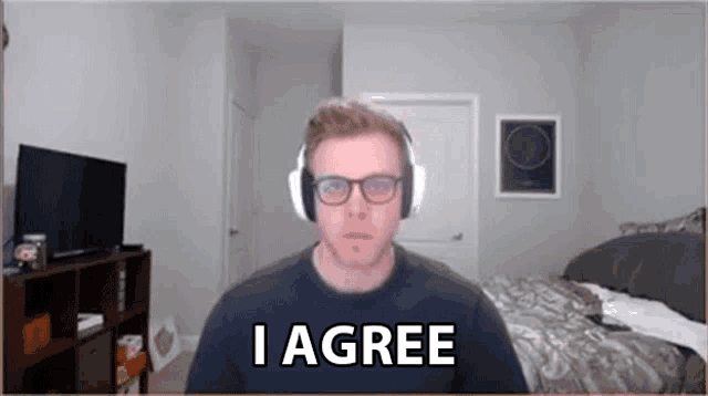 a man wearing headphones and glasses says i agree in a bedroom