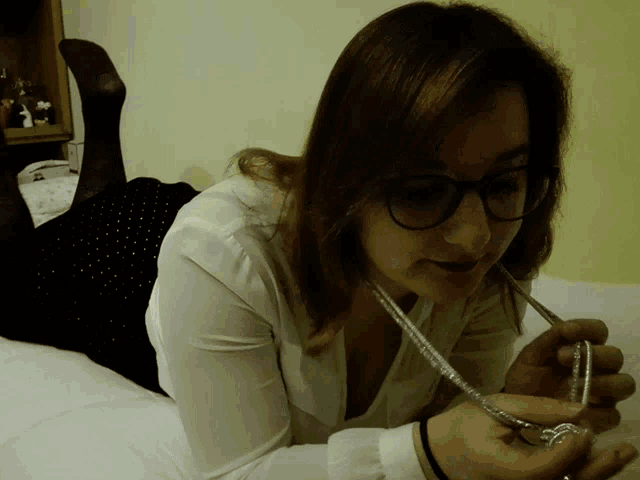 a woman wearing glasses is laying on a bed and holding a necklace