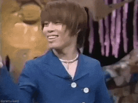 a young man in a blue suit and a necklace is smiling while standing in front of a statue .