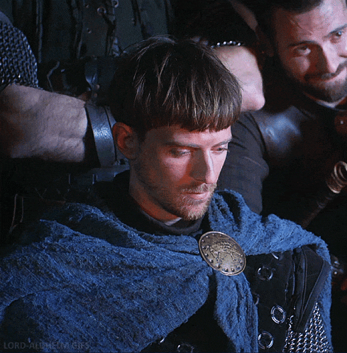 a man wearing a blue cape with a gold buckle on it looks down at something