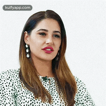 a close up of a woman wearing a white and green polka dot shirt and earrings .