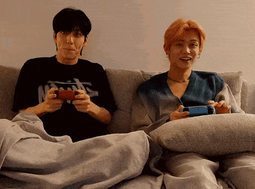 two men are sitting on a couch holding video games .