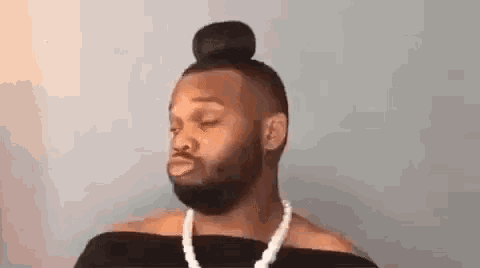 a man with a bun on his head is wearing a pearl necklace and a black top .