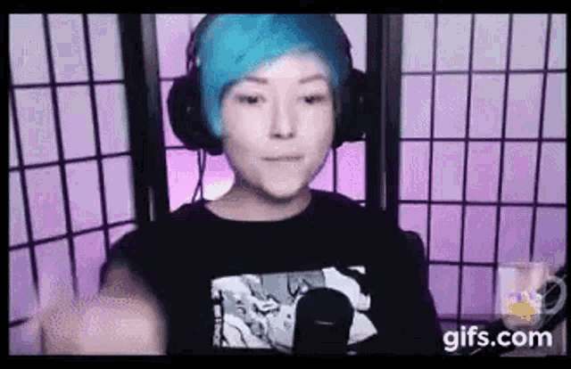 a person with blue hair and headphones is standing in front of a microphone .