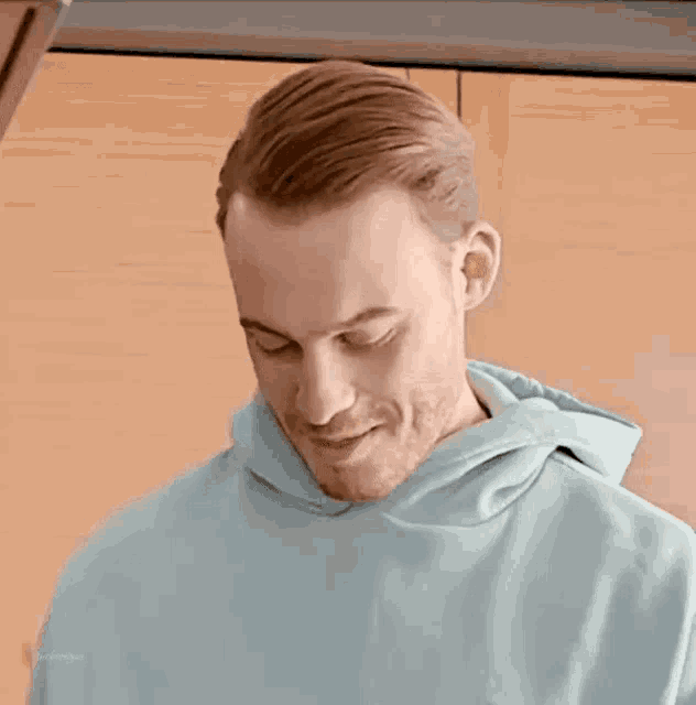 a man in a blue hoodie is smiling and looking down at something .