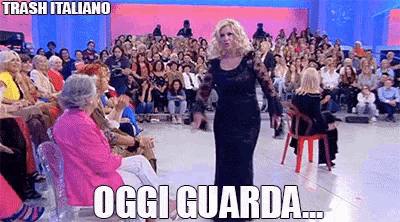 a woman in a black dress stands in front of a crowd of people and says oggi guarda