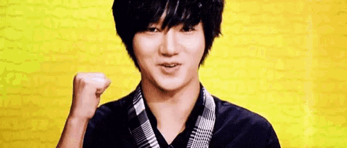 a young man is holding his fist up in the air in front of a yellow wall .