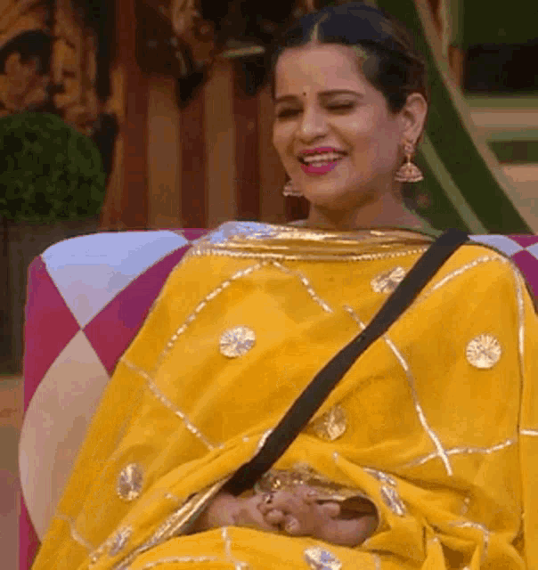 a woman in a yellow saree is smiling while sitting on a chair
