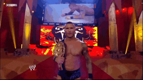 a man is holding a wrestling championship belt in front of a screen that says wwe