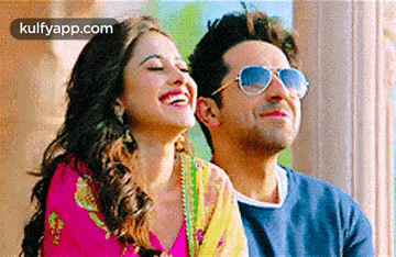 a man and a woman are standing next to each other and smiling . the man is wearing sunglasses .