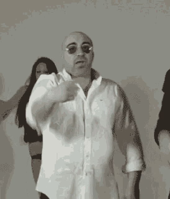 a bald man in a white shirt and sunglasses is dancing with a group of women .