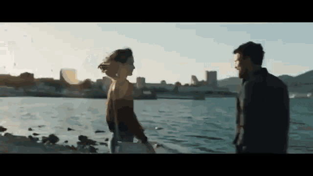 a man and a woman are standing next to each other on a beach near the water .