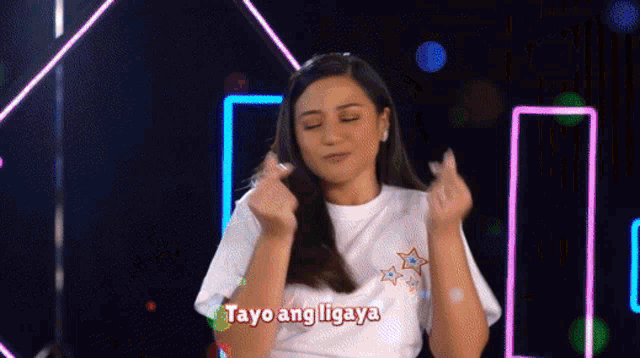 a woman in a white shirt is making a heart shape with her hands and the words " tayo ang ibigay " written on her shirt