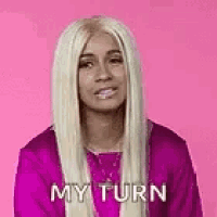 a woman with long blonde hair is wearing a purple shirt and a wig and says `` my turn '' .