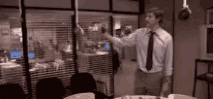 a man in a tie is standing in front of a window in an office holding a cup .