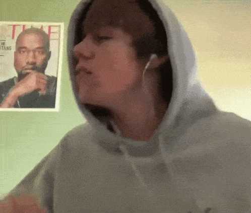 a man wearing a hoodie and ear buds is standing in front of a time magazine poster