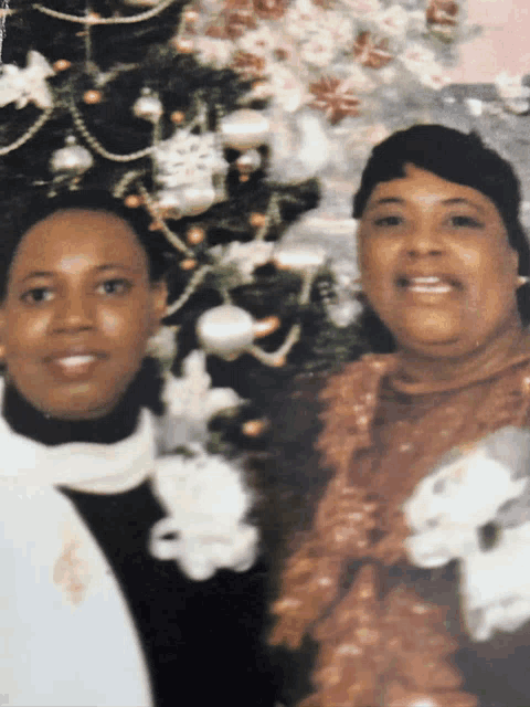 two women are posing in front of a christmas tree