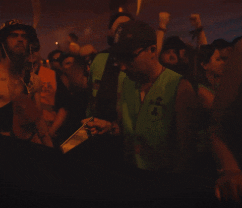 a man wearing a green vest with the letter k on it stands in front of a crowd