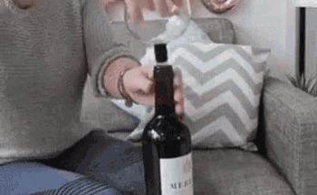 a woman is sitting on a couch opening a bottle of wine .