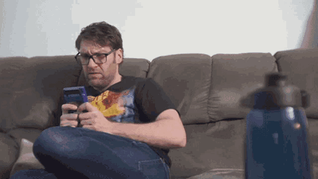 a man wearing glasses is sitting on a couch playing a game boy