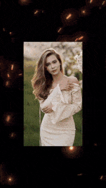a woman in a white dress is standing in a field with flowers in the background