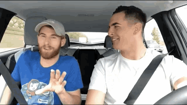 two men in a car one wearing a blue shirt that says paradise on it