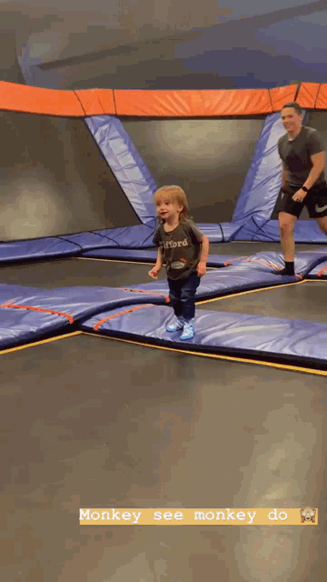 a little boy is jumping on a trampoline while a man watches