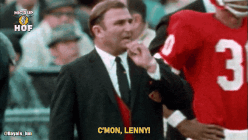 a man in a suit and tie is talking to a football player wearing a red jersey with the number 3 on it