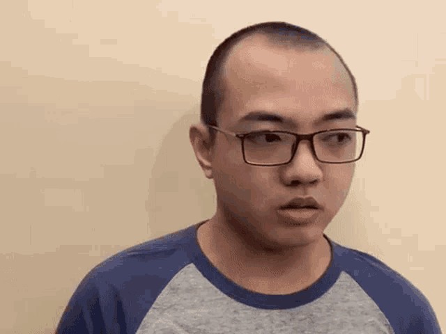 a man with glasses and a shaved head is standing in front of a wall .