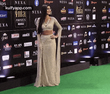 a woman in a white dress is standing on a green carpet in front of a wall with advertisements for nexa .