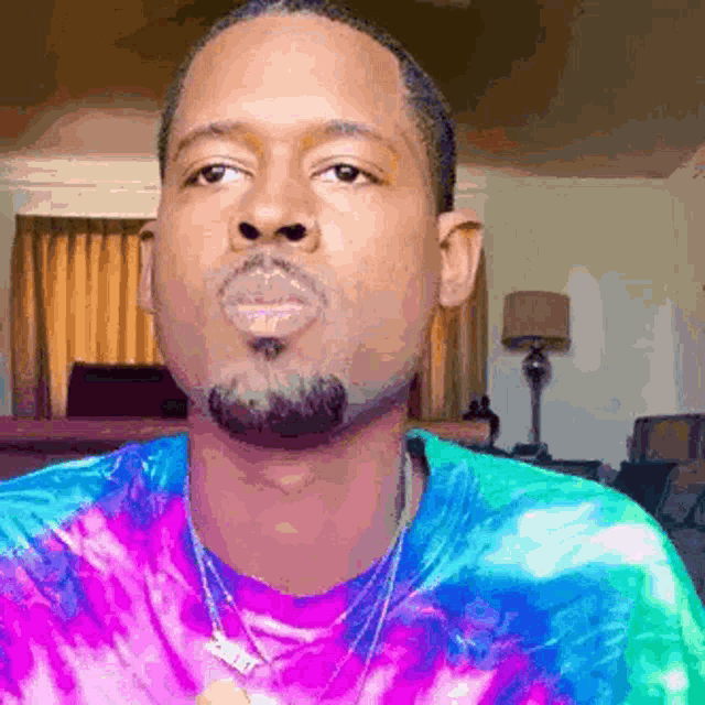 a man with a beard and a tie dye shirt is making a funny face .