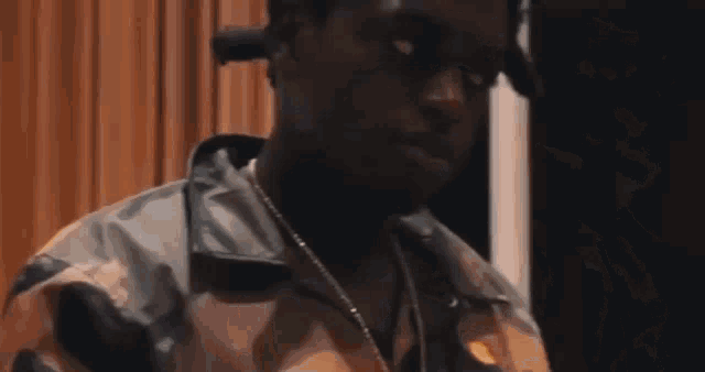 a man wearing a camouflage jacket and a necklace is standing in front of a curtain .