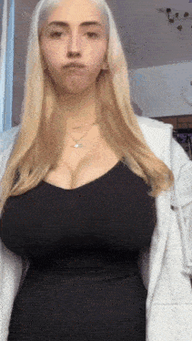 a woman with very large breasts is wearing a black dress and a grey jacket .