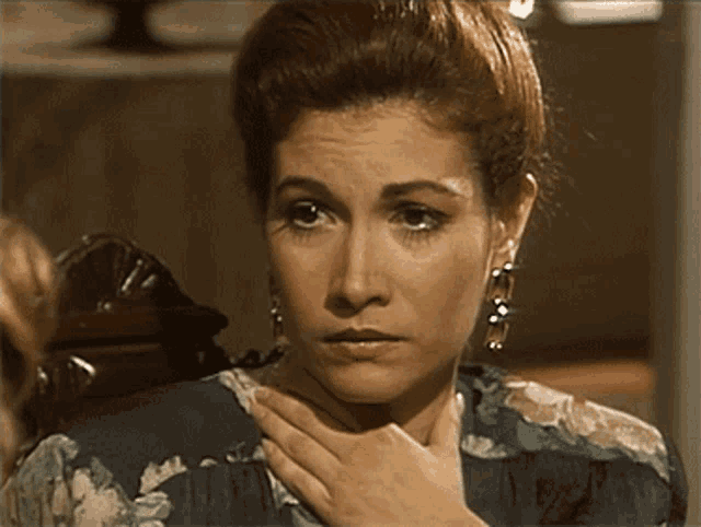 a woman holds her hand to her throat while wearing earrings