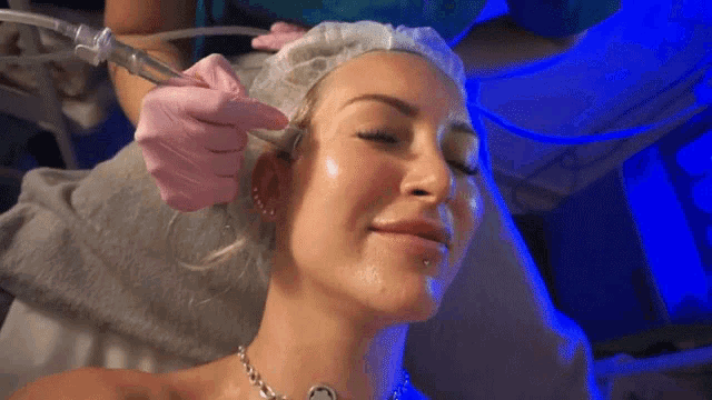 a woman is getting a treatment on her face with a blue light behind her