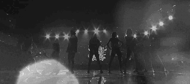 a black and white photo of a group of people dancing on a stage with lights .