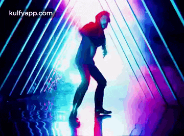 a man is dancing in a dark room with purple and blue lights behind him .