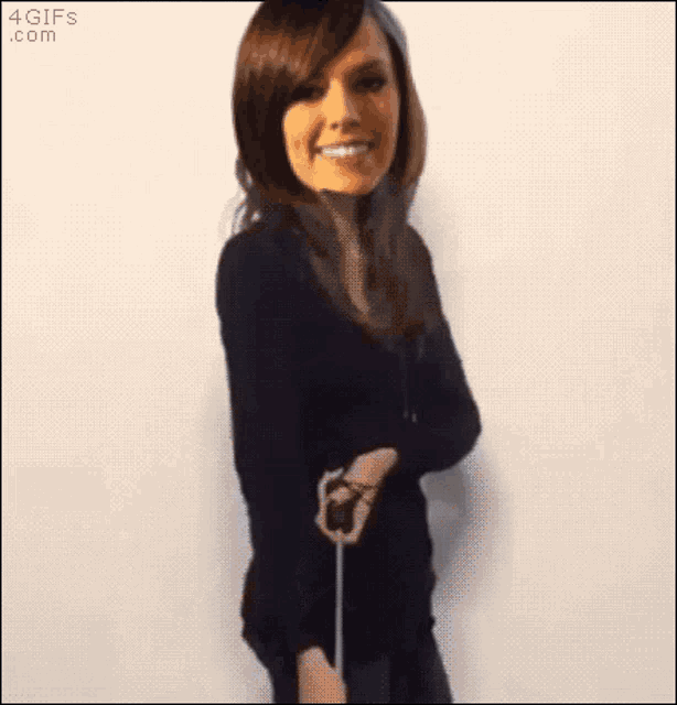a woman in a black shirt is smiling and holding a stick in front of a white wall with the website 4gifs.com visible