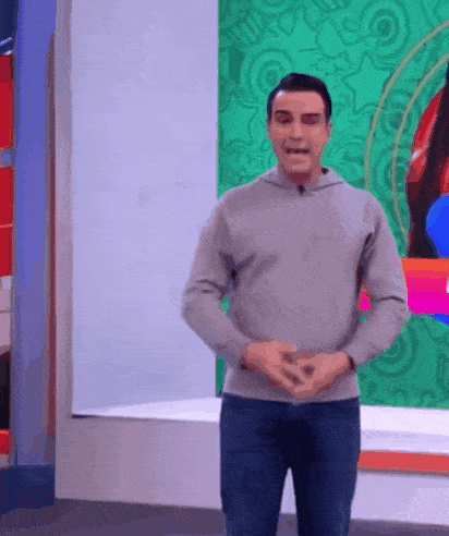 a man in a gray sweater and jeans is standing in front of a green wall