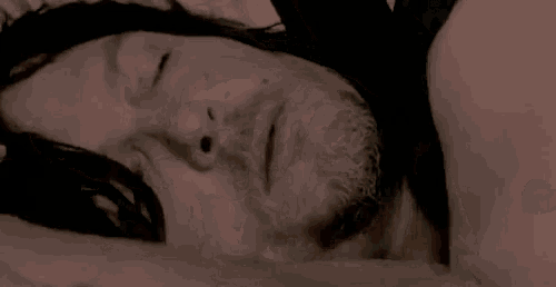 a woman is laying on a bed with her eyes closed and a hand on her head .