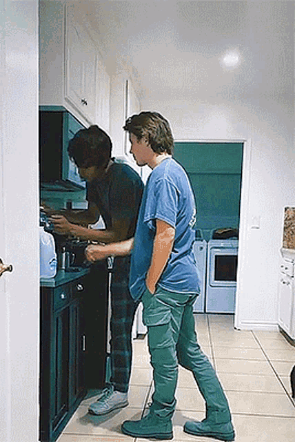 two men are standing in a kitchen one is wearing a blue shirt that says ' california ' on it