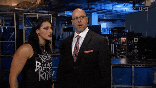 a man in a suit and tie stands next to a woman wearing a black tank top that says " black reign "