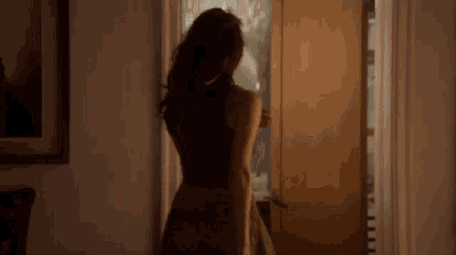a woman in a dress is standing in a doorway looking out the window .