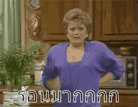 a woman in a purple shirt is standing in a kitchen with a microwave .