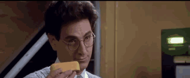 a man wearing glasses is holding a piece of cheese .