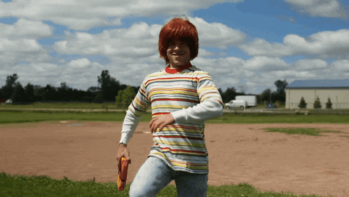 a person wearing a striped shirt and a red wig is standing in a field