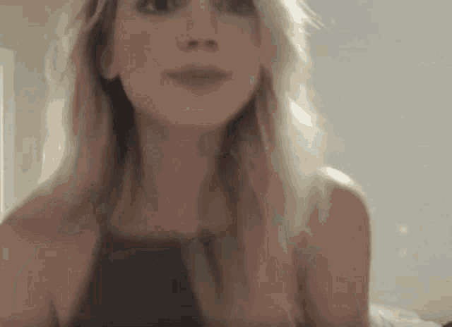 a woman with long blonde hair is wearing a black tank top and making a funny face .